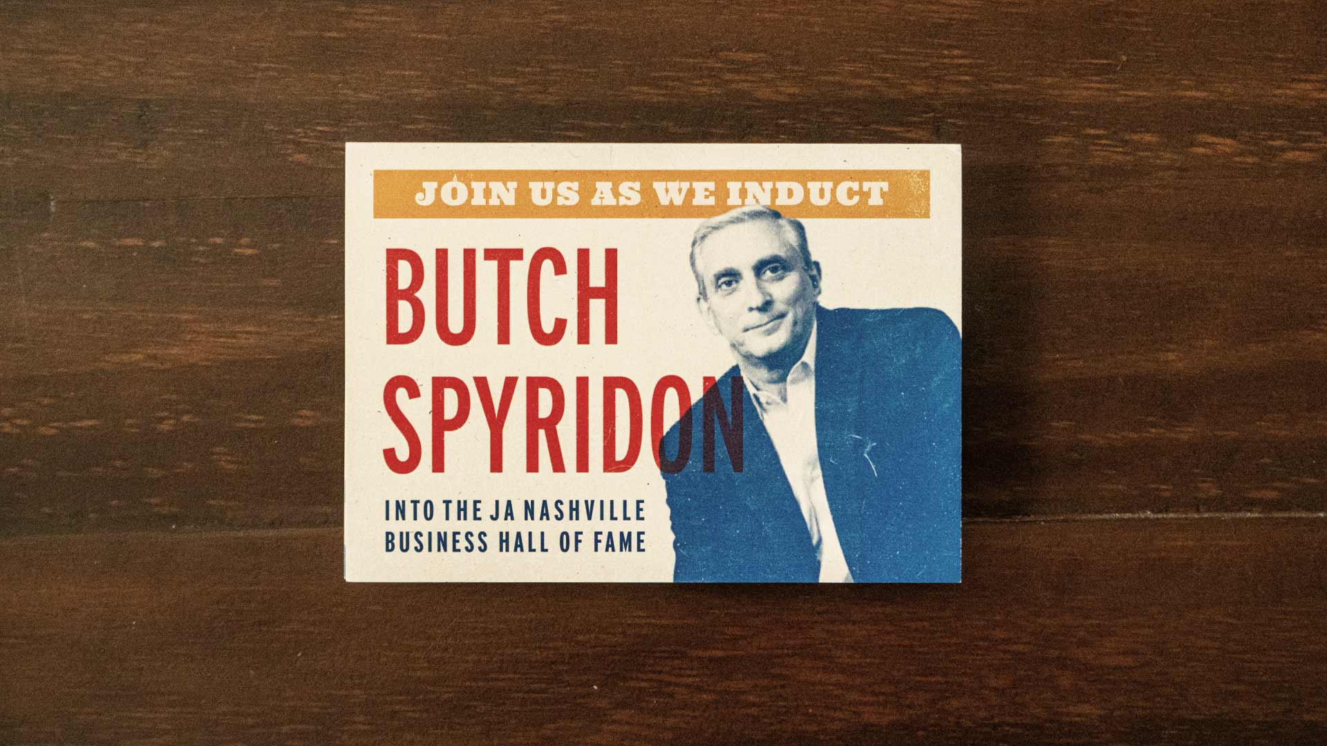 Folded invitation with Butch Spyridon's photo on a dark wood background