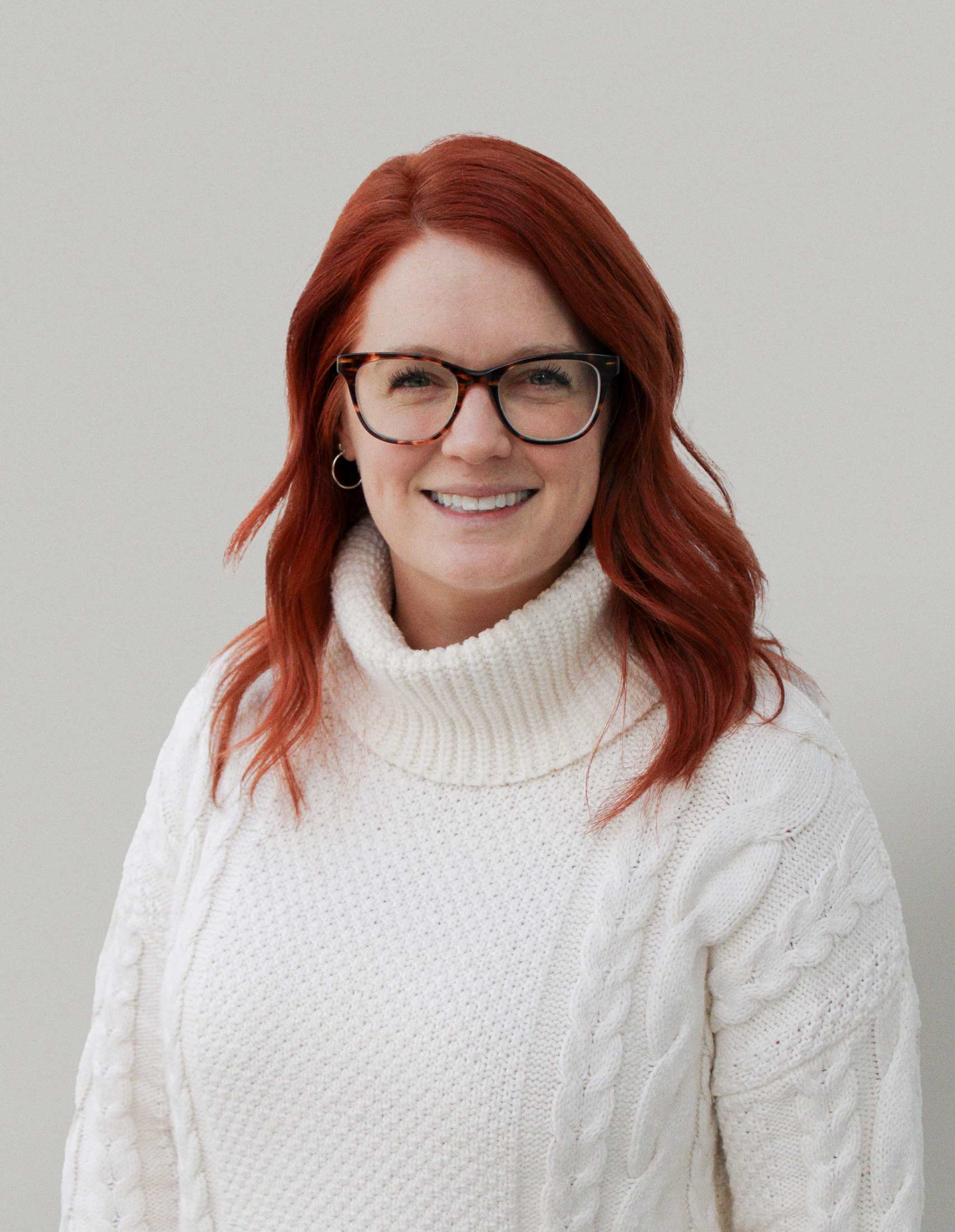 Project and Account Manager, white sweater with red hair and glasses looking at camera