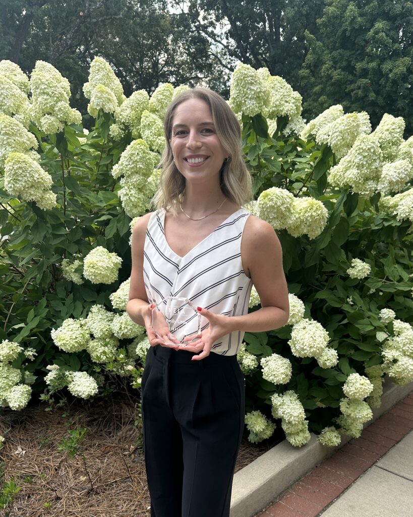 Emily Little holding her award in front of a blooming hydrangea bush.